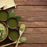 Préparation du matcha : poudre verte, fouet en bambou, bols de thé et cuillères en bois sur une table en bois.