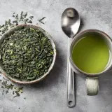 Thé vert en vrac dans un bol, une tasse de thé vert et une cuillère. Le thé vert est connu pour ses bienfaits, mais il peut aussi avoir des egcg effets secondaires.