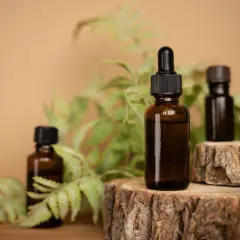 Flacons d'huile essentielle sur des rondins de bois, entourés de verdure. Une solution naturelle pour soulager le mal de gorge.