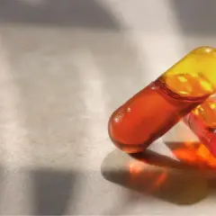 Deux capsules d'huile de krill translucides, aux teintes orangées et jaunes, sur une surface texturée. Découvrez les bienfaits de l'huile de krill.