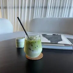Un verre de thé matcha glacé, crémeux et rafraîchissant, avec une paille noire, à côté d'une boîte de matcha et d'un livre.