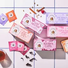 Des boîtes de thé colorées, dont un thé noir "Le Réveille?", disposées sur un carrelage blanc, avec des épices et des fruits rouges.