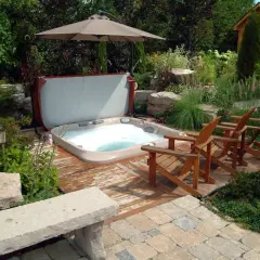 Aménagement spa gonflable dans un jardin luxuriant avec des chaises en bois, un parasol et une petite cabane en bois.