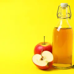 Bouteille de vinaigre de cidre et pommes rouges, suggérant un urticaire traitement naturel.