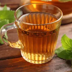 Une tasse de thé ambré, ornée de feuilles de mélisse fraîche, sur une table en bois.