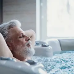 Un homme âgé se détend dans un jacuzzi, les yeux fermés. Il semble si paisible, on se demande si on peut faire du spa tous les jours.