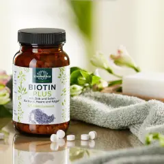 Bouteille de Biotin Plus, un supplément de vitamine B7, entourée de fleurs et d'une serviette douce. Idéal pour la peau, les cheveux et les ongles.