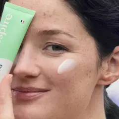 Une femme applique une crème hydratante sur sa joue. Le tube "Respire" est tenu près de son visage, montrant comment hydrater sa peau.