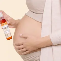 Une femme enceinte tient une huile de soin pour vergetures, idéale pour la grossesse. Le rooibos, ingrédient naturel, prend soin de la peau.