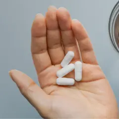 Main ouverte tenant des gélules blanches pour une cure de zinc, à côté d'un verre d'eau.
