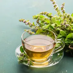 Une tasse de tisane dorée, prête à être dégustée, avec un bouquet de menthe fraîche. Le temps infusion tisane est parfait.