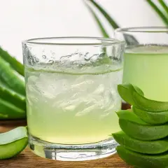 Deux verres de jus d'aloe vera à boire, entourés de feuilles d'aloe vera fraîches et de morceaux coupés.