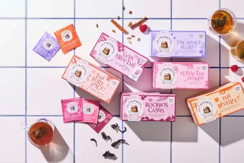 Des boîtes de thé colorées, dont un thé noir "Le Réveille?", disposées sur un carrelage blanc, avec des épices et des fruits rouges.