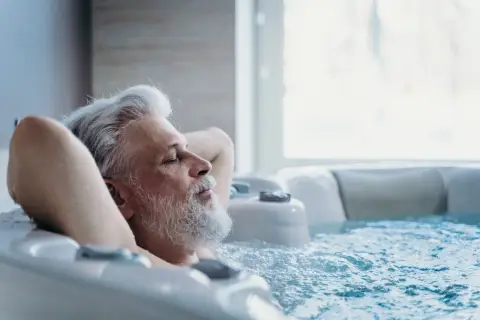Un homme âgé se détend dans un jacuzzi, les yeux fermés. Il semble si paisible, on se demande si on peut faire du spa tous les jours.