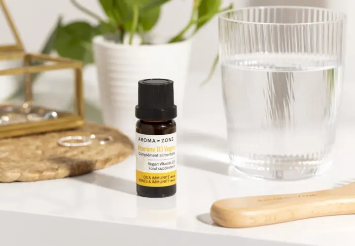 Un remède de grand-mère pour le manque de vitamine D : un flacon de Vitamine D3 Vegan Aroma-Zone, à côté d'un verre d'eau et d'une brosse en bois.