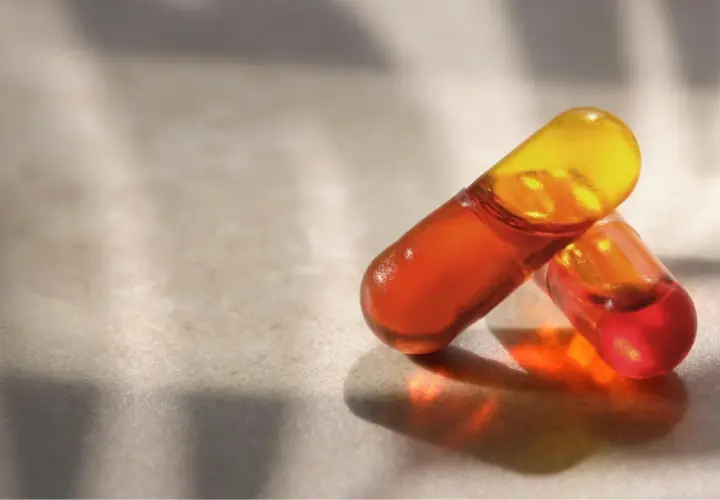Deux capsules d'huile de krill translucides, aux teintes orangées et jaunes, sur une surface texturée. Découvrez les bienfaits de l'huile de krill.
