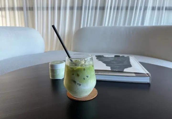 Un verre de thé matcha glacé, crémeux et rafraîchissant, avec une paille noire, à côté d'une boîte de matcha et d'un livre.
