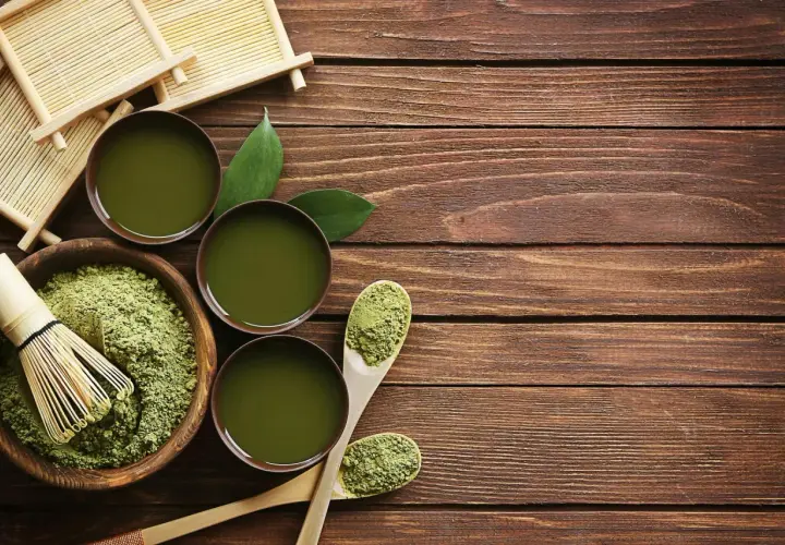 Préparation du matcha : poudre verte, fouet en bambou, bols de thé et cuillères en bois sur une table en bois.