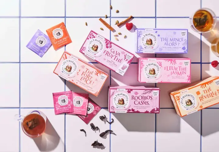 Des boîtes de thé colorées, dont un thé noir "Le Réveille?", disposées sur un carrelage blanc, avec des épices et des fruits rouges.