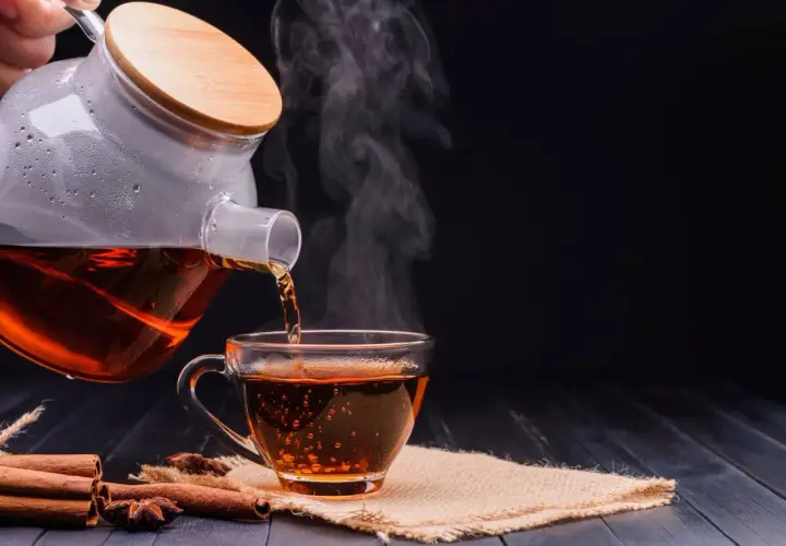 Un thé noir fumant est versé d'une théière en verre dans une tasse. Parfait pour un moment de détente avant le sommeil.