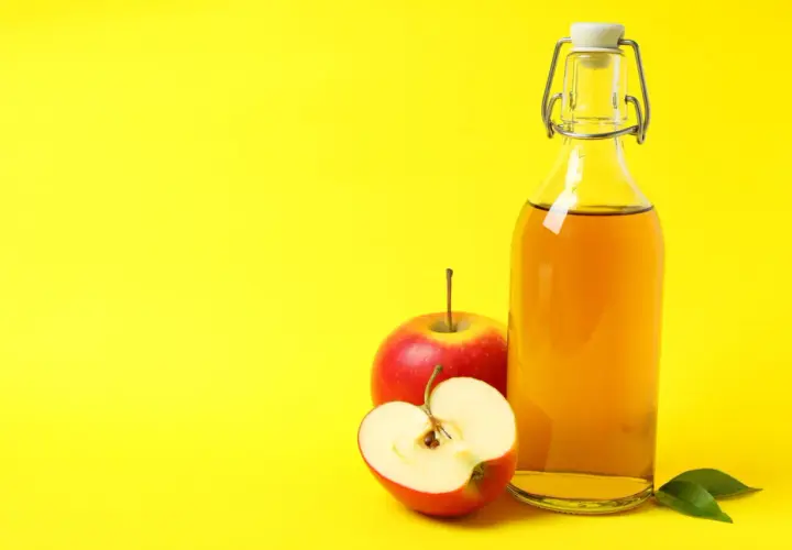 Bouteille de vinaigre de cidre et pommes rouges, suggérant un urticaire traitement naturel.