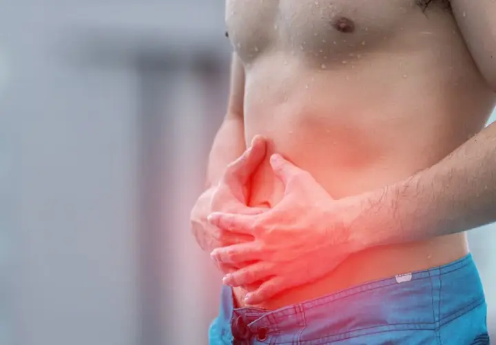 Homme tenant son ventre douloureux, cherchant comment calmer les douleurs d'estomac. La zone rouge indique la douleur.