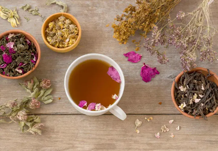 Tasses de thé aux herbes et pétales de rose, idéales pour apaiser la nausée. Des herbes séchées et des fleurs décorent la table en bois.