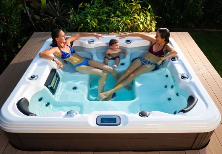 Deux femmes et un bébé profitent du bienfait jacuzzi en extérieur, entourés de verdure.
