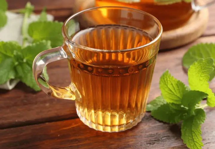Une tasse de thé ambré, ornée de feuilles de mélisse fraîche, sur une table en bois.