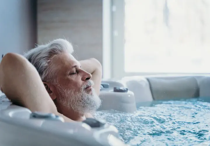 Un homme âgé se détend dans un jacuzzi, les yeux fermés. Il semble si paisible, on se demande si on peut faire du spa tous les jours.