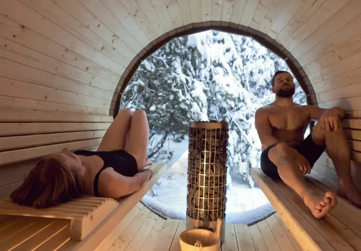 Couple se détendant dans un sauna en bois, avec vue sur une forêt enneigée. Le sauna tous les jours danger, mais ici, c'est un moment de pur bien-être.