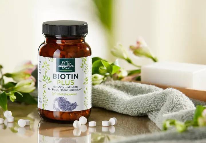 Bouteille de Biotin Plus, un supplément de vitamine B7, entourée de fleurs et d'une serviette douce. Idéal pour la peau, les cheveux et les ongles.