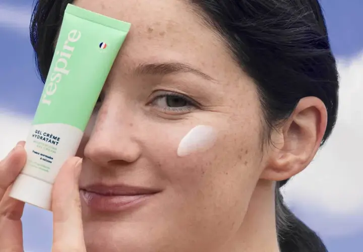 Une femme applique une crème hydratante sur sa joue. Le tube "Respire" est tenu près de son visage, montrant comment hydrater sa peau.