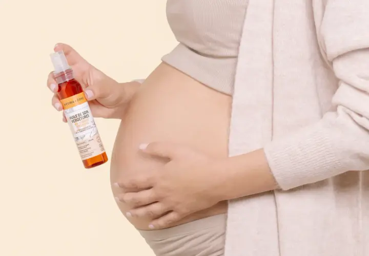 Une femme enceinte tient une huile de soin pour vergetures, idéale pour la grossesse. Le rooibos, ingrédient naturel, prend soin de la peau.