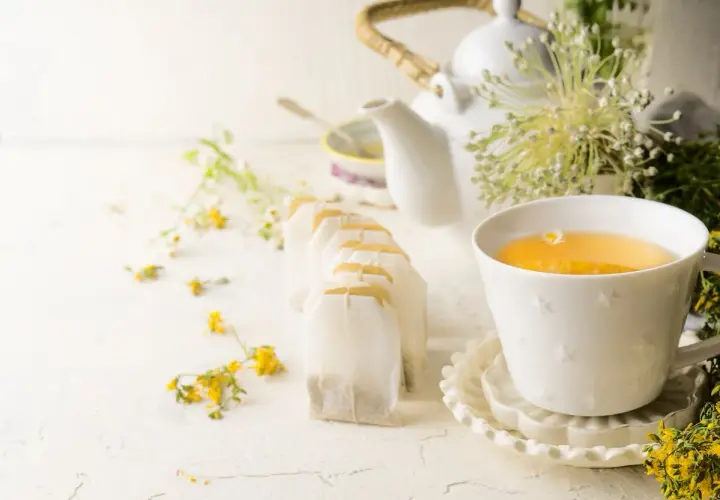 Une tasse de thé ou tisane pour la santé, entourée de fleurs sauvages et de sachets de thé.