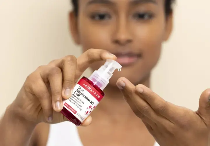 Une goutte de sérum à l'acide glycolique tombe d'une pipette sur le doigt d'une femme.