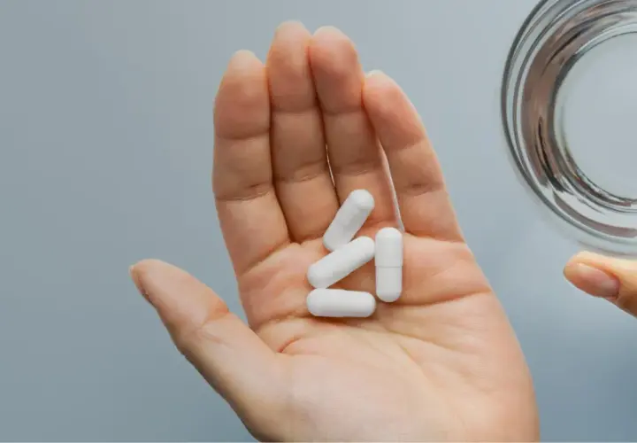 Main ouverte tenant des gélules blanches pour une cure de zinc, à côté d'un verre d'eau.