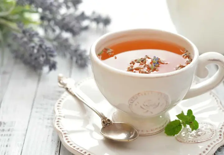 Une tasse de thé à la lavande, parfaite pour savoir quel thé boire le soir. Une cuillère ancienne et des brins de menthe complètent la scène.