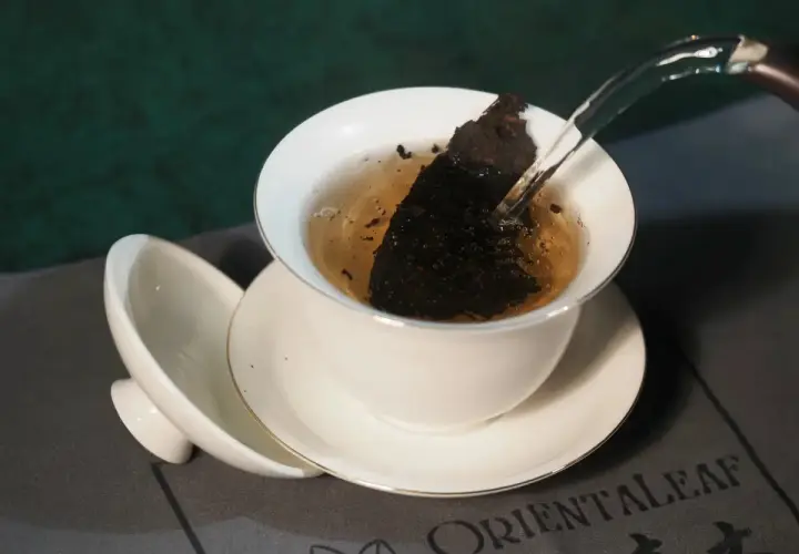 Infusion d'un thé sombre dans une tasse blanche, révélant les fermenté bienfaits. L'eau chaude libère les arômes.