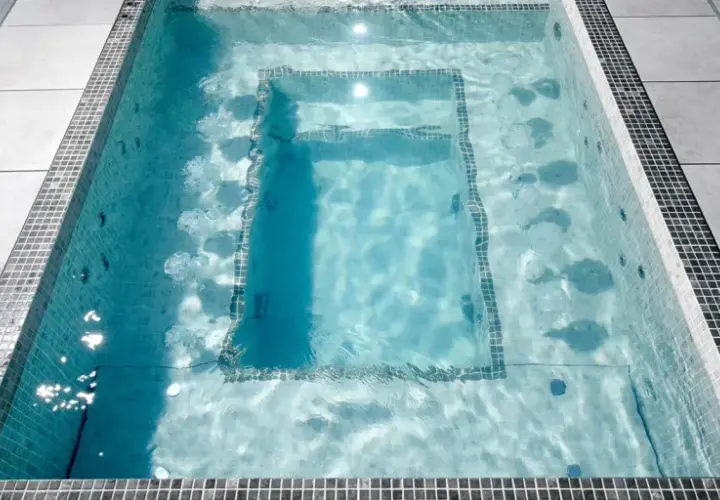 Un jacuzzi moderne avec des jets d'eau, entouré de carrelage et de dalles grises. Le poids d'un jacuzzi rempli d'eau est considérable.