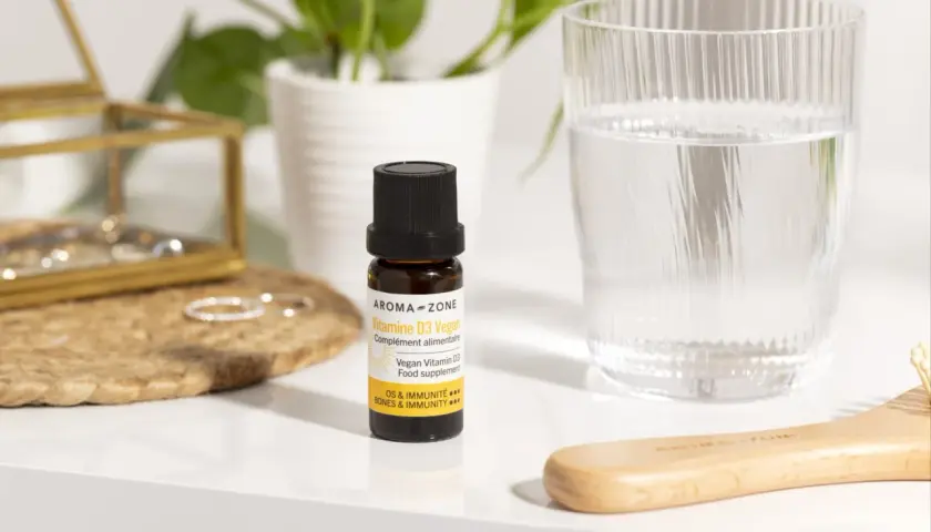 Un remède de grand-mère pour le manque de vitamine D : un flacon de Vitamine D3 Vegan Aroma-Zone, à côté d'un verre d'eau et d'une brosse en bois.