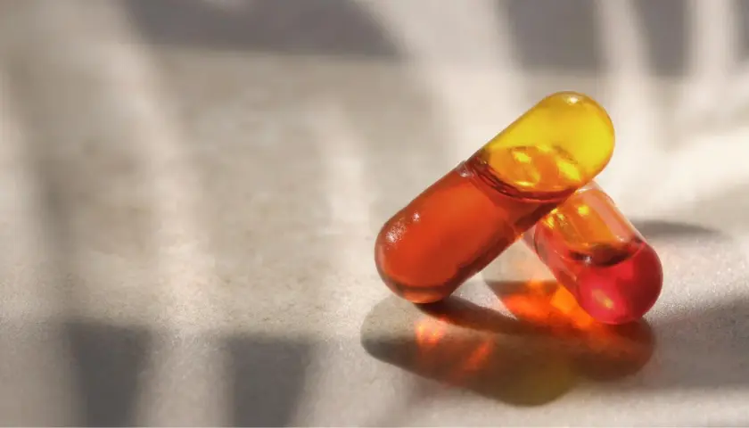 Deux capsules d'huile de krill translucides, aux teintes orangées et jaunes, sur une surface texturée. Découvrez les bienfaits de l'huile de krill.