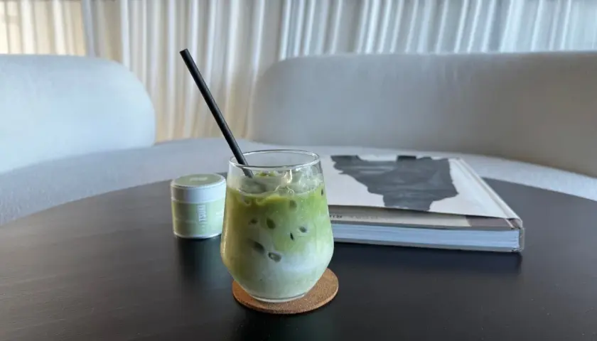 Un verre de thé matcha glacé, crémeux et rafraîchissant, avec une paille noire, à côté d'une boîte de matcha et d'un livre.