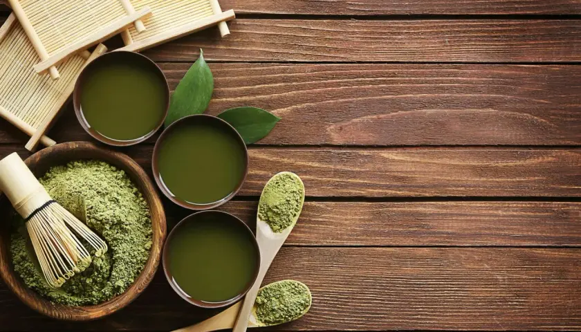 Préparation du matcha : poudre verte, fouet en bambou, bols de thé et cuillères en bois sur une table en bois.
