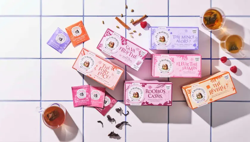 Des boîtes de thé colorées, dont un thé noir "Le Réveille?", disposées sur un carrelage blanc, avec des épices et des fruits rouges.