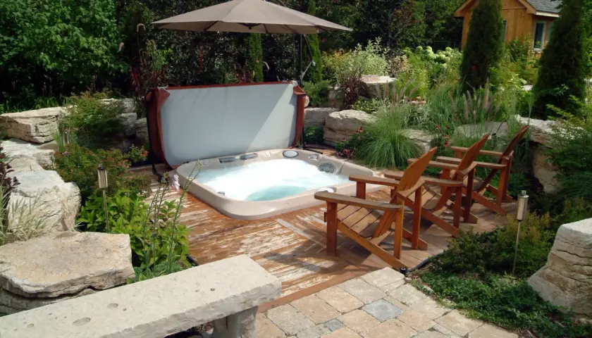 Aménagement spa gonflable dans un jardin luxuriant avec des chaises en bois, un parasol et une petite cabane en bois.