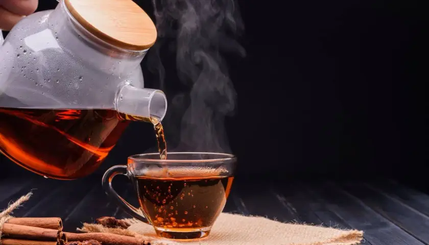 Un thé noir fumant est versé d'une théière en verre dans une tasse. Parfait pour un moment de détente avant le sommeil.