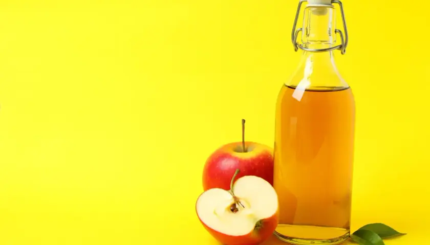 Bouteille de vinaigre de cidre et pommes rouges, suggérant un urticaire traitement naturel.
