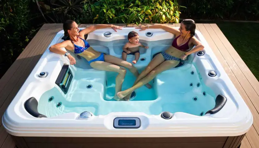 Deux femmes et un bébé profitent du bienfait jacuzzi en extérieur, entourés de verdure.