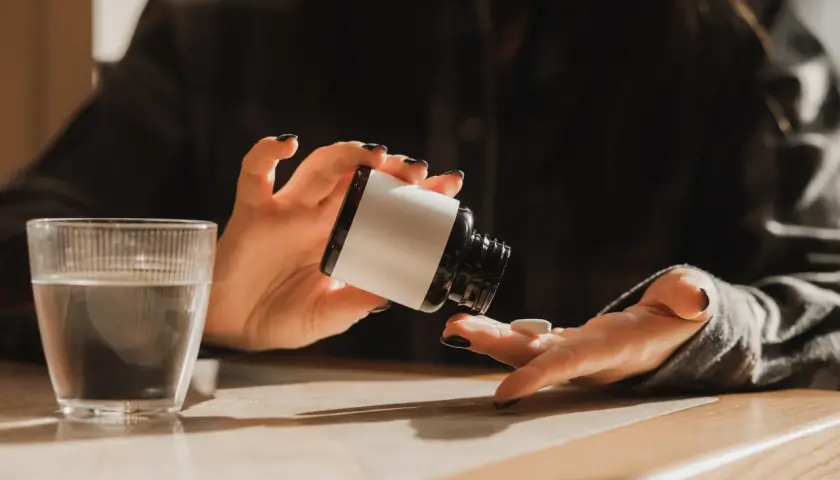 Une personne prend un comprimé de magnésium, prêt à commencer sa cure. Un verre d'eau est à proximité.
